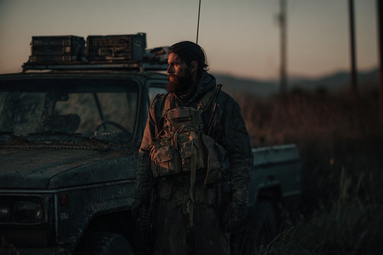 A capable civilian beside a vehicle rigged with radio equipment at dusk